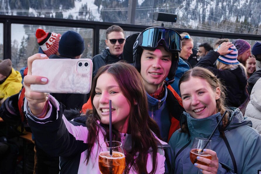 Young people taking a selfie with drinks in the snow.