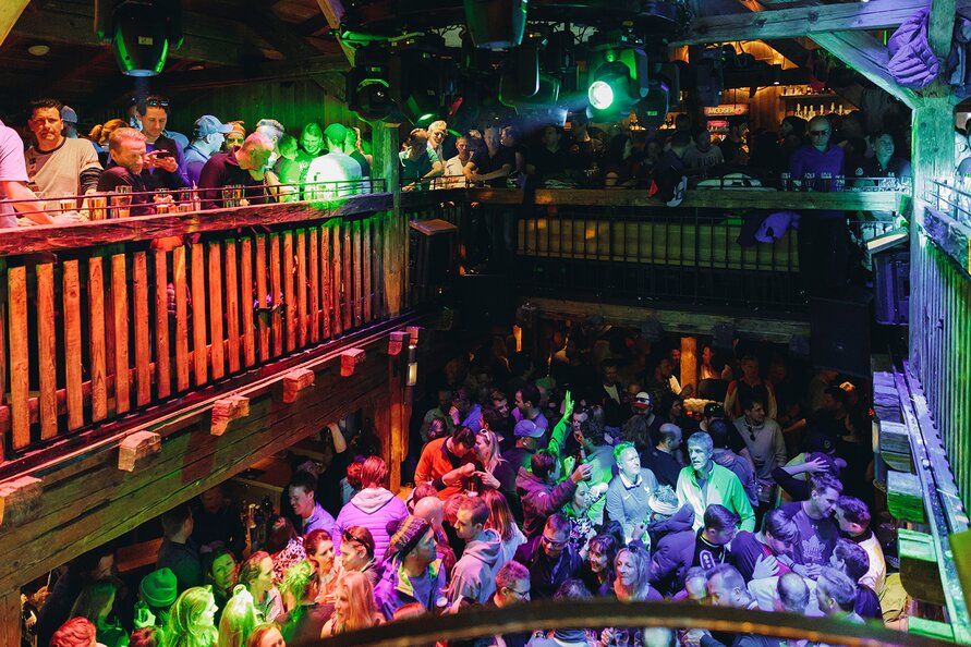 Crowd partying on two floors in a rustic bar.