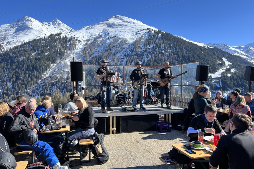 Mountain scenery with band, snowy peaks, and outdoor audience.