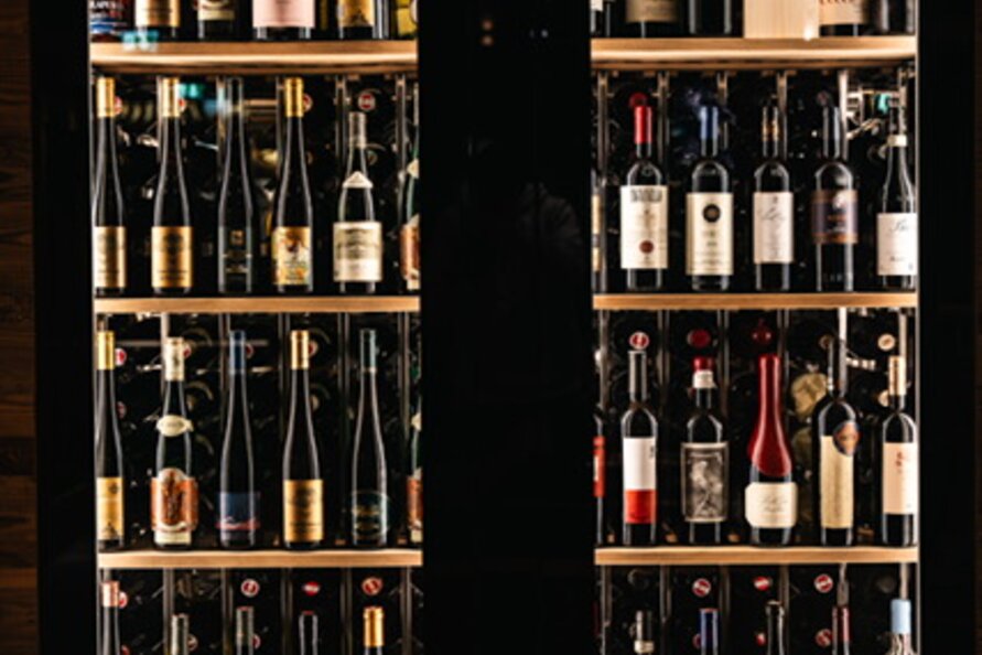 A well-stocked wine cooler with various bottles.