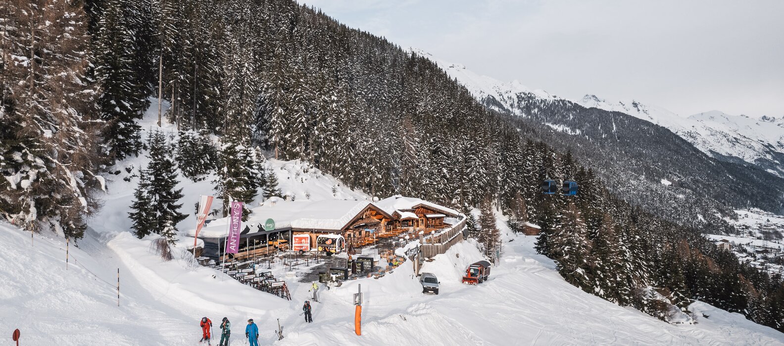 Winter landscape with skiers in front of a mountain lodge in the snow.