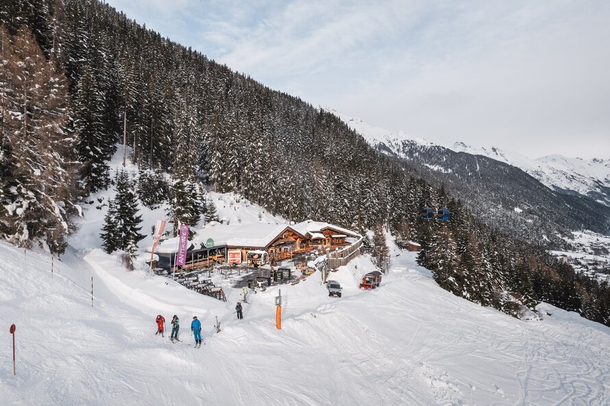 Winter landscape with skiers in front of a mountain lodge in the snow.