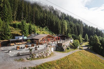 Eine Berghütte inmitten eines Waldes mit Terrasse und Sonnenschirmen.