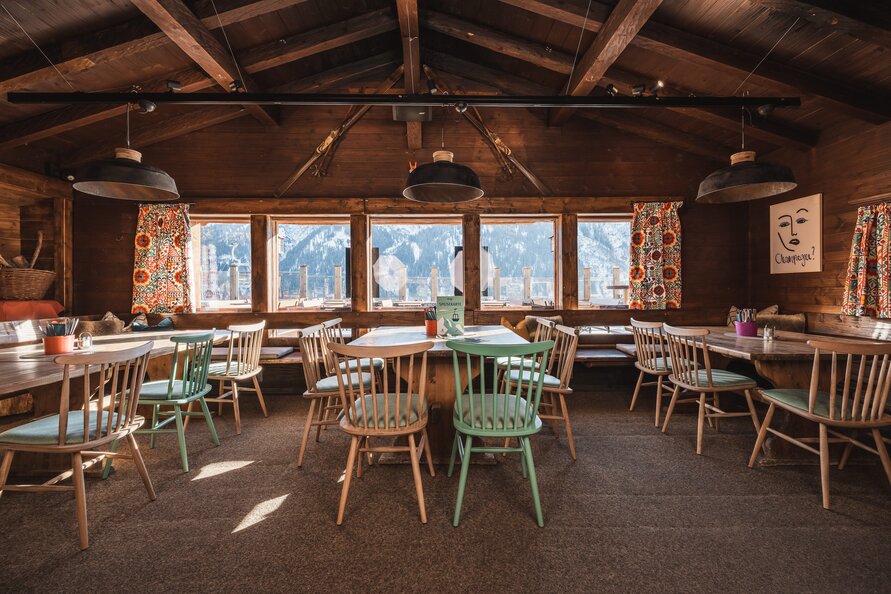 Interior of an alpine hut with wooden decor and a view of snowy mountains through the windows.