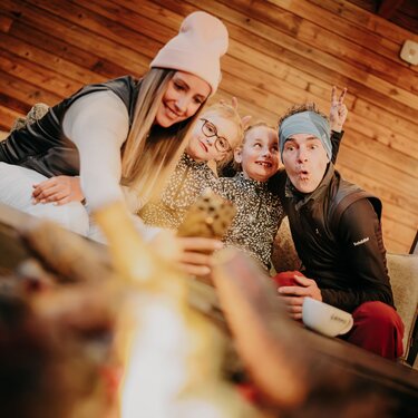 Family taking a selfie in front of a fireplace in a cozy setting.