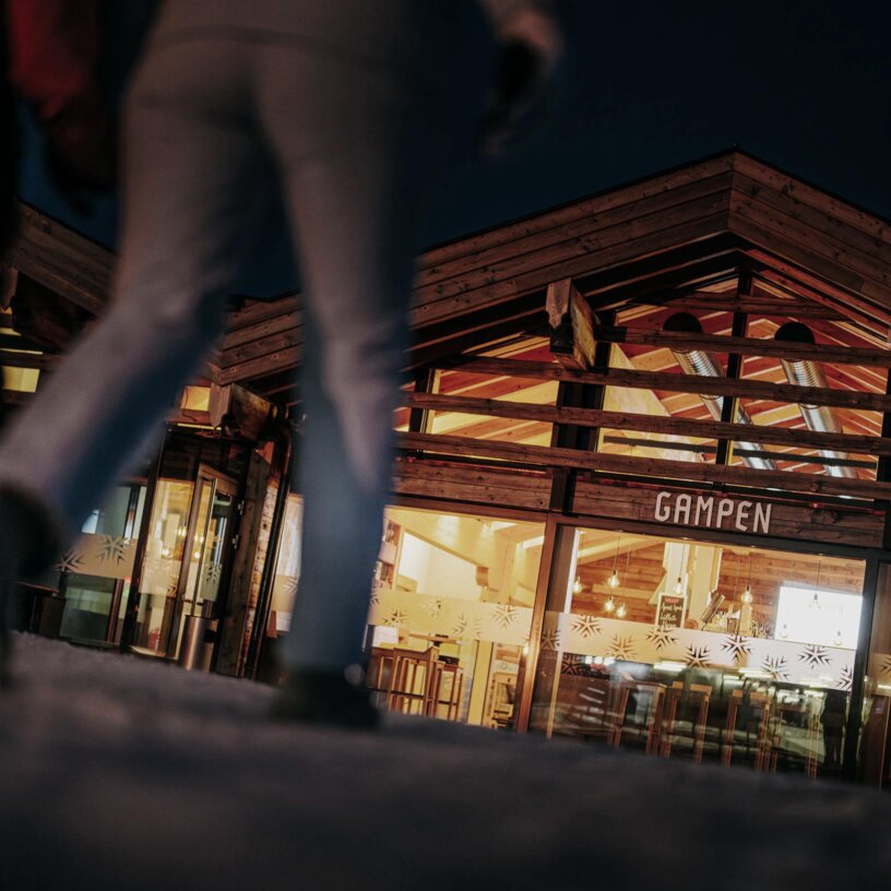 Two people walking towards a lit restaurant called Gampen.