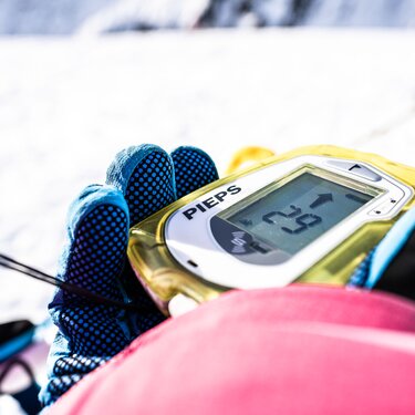 Close-up of avalanche transceiver showing '2.5' in a snowy setting.