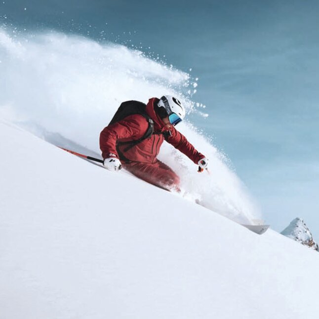 Ein Freerider fährt in rotem Skianzug einen Tiefschnee-Hang in St. Anton am Arlberg hinunter.