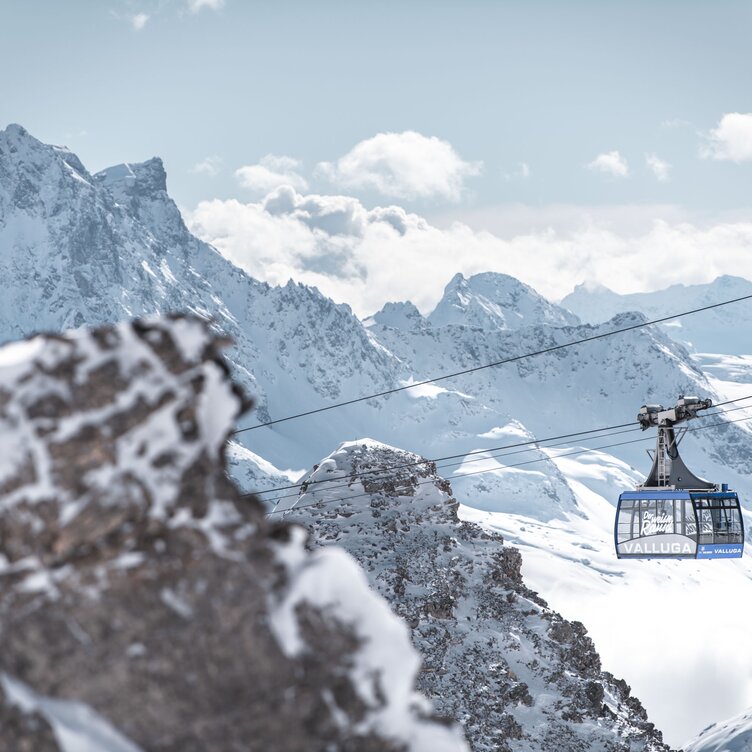 Eine Seilbahn schwebt über schneebedeckte Berge in den Alpen.