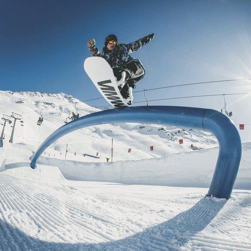 Ein Snowboarder slidet über einen blauen Railbogen im stanton park.
