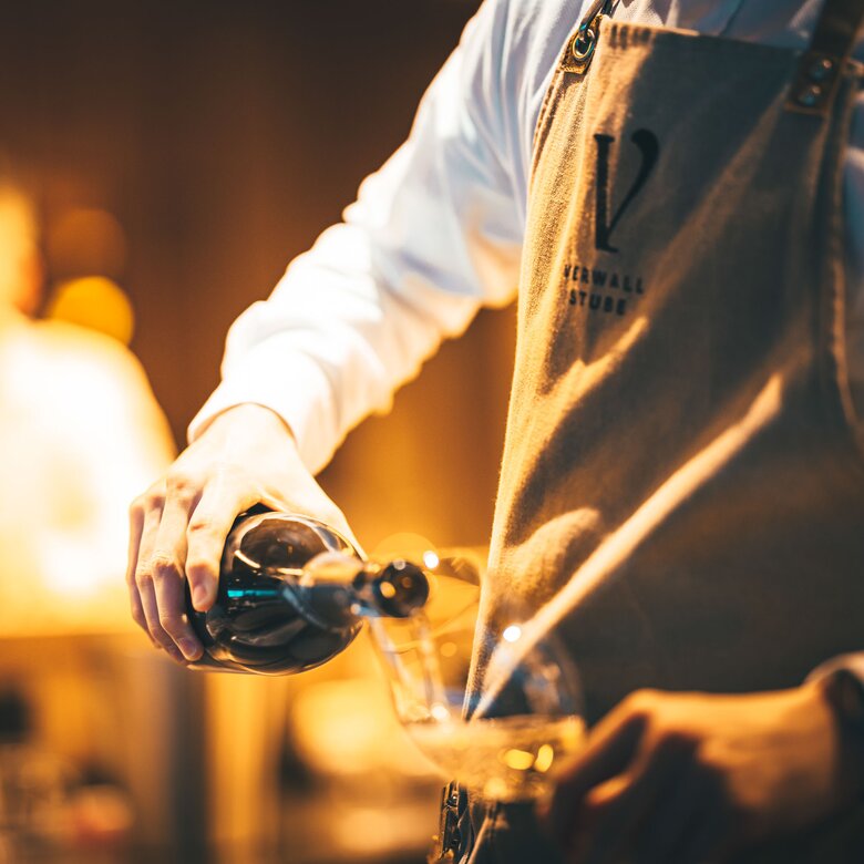 A waiter pours wine into a glass by candlelight.
