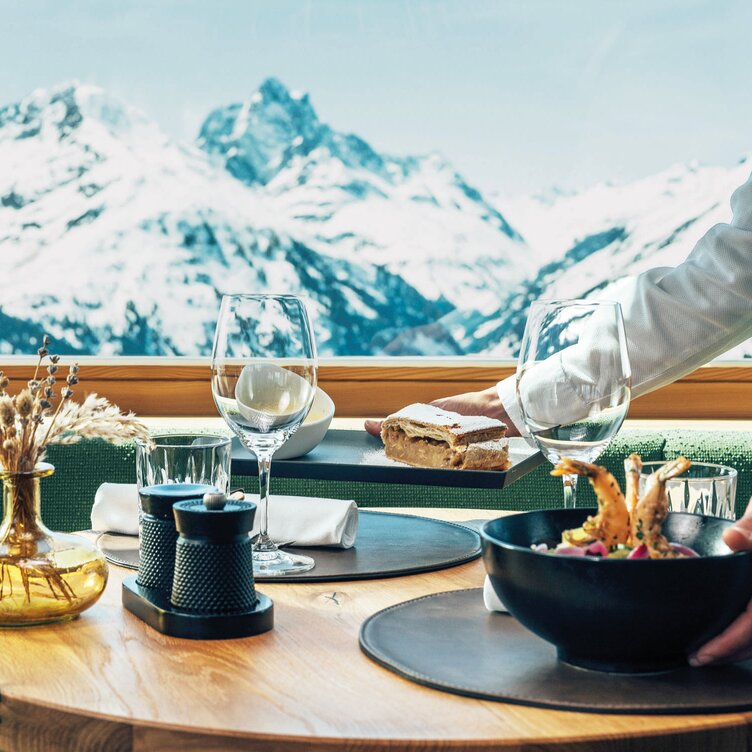 Table set for lunch with mountain view; server placing a plate.