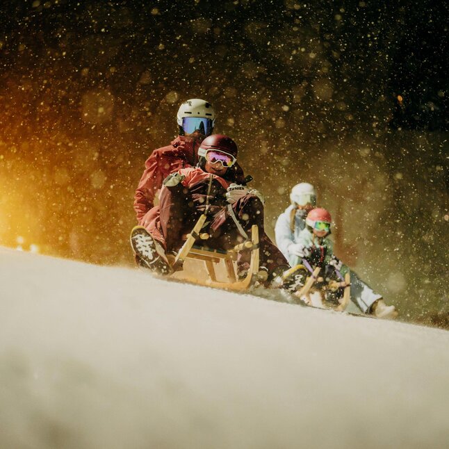 Menschen rodeln im Schnee während der Abenddämmerung.