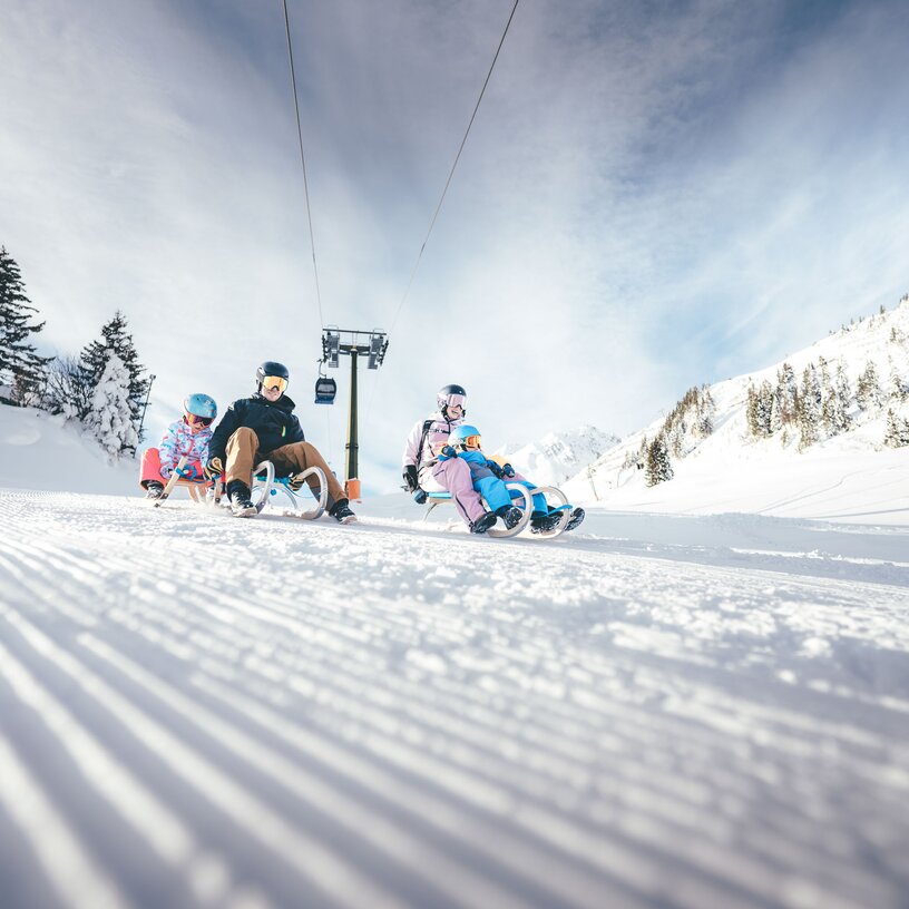 Three people sledding in a snowy mountain landscape.