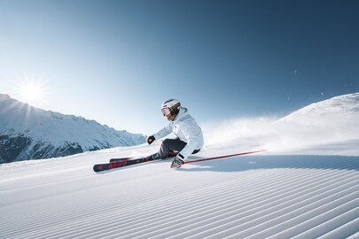 Skifahrer carvt bei Sonnenaufgang auf frisch präparierter Piste.