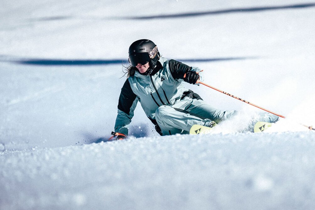 A skier in full gear making a dynamic turn through powder snow.