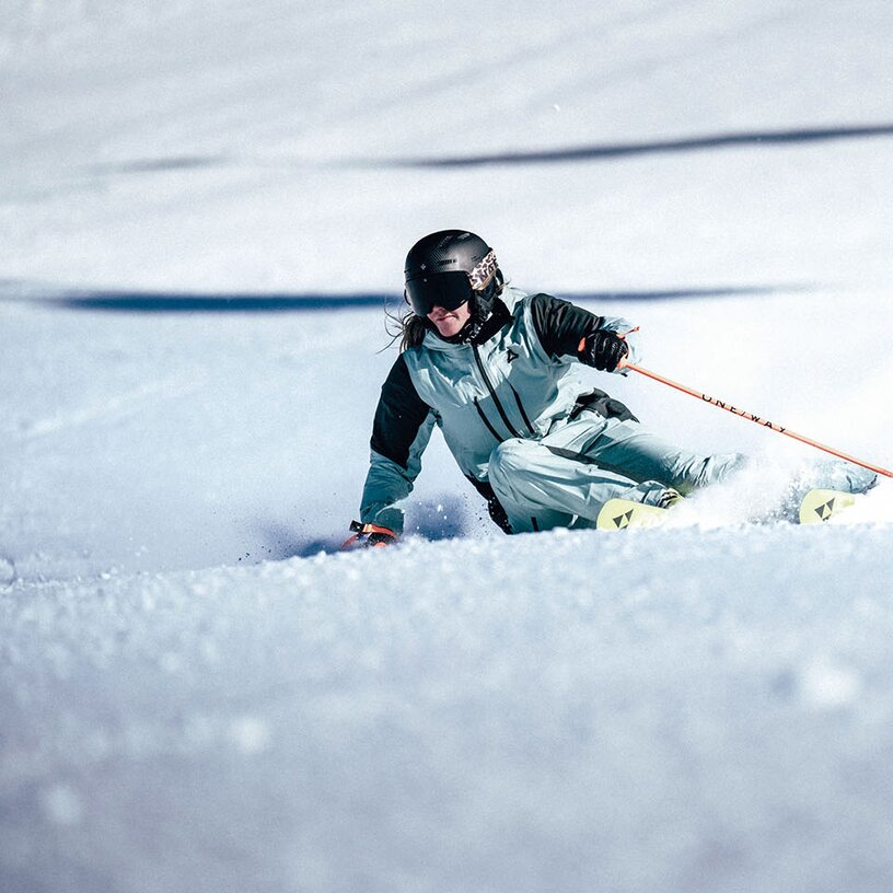 A skier in full gear making a dynamic turn through powder snow.