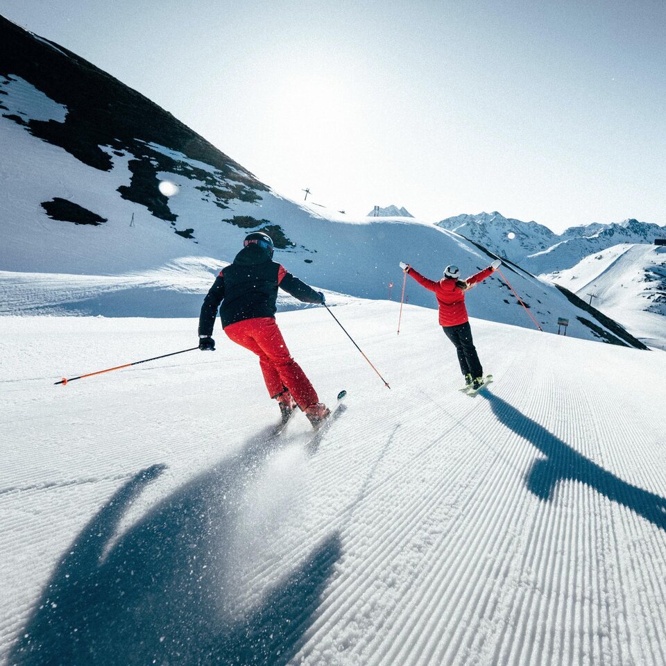Two skiers on a sunny slope surrounded by mountains.