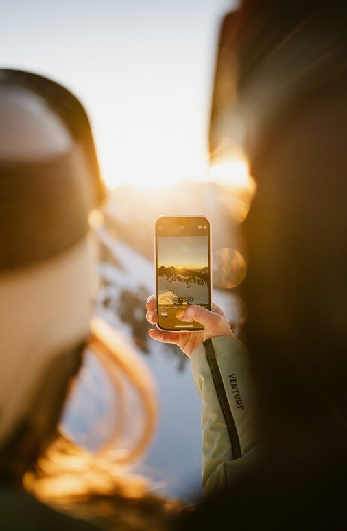 Zwei Personen fotografieren mit dem Smartphone den Sonnenuntergang in der Skiregion St. Anton am Arlberg.