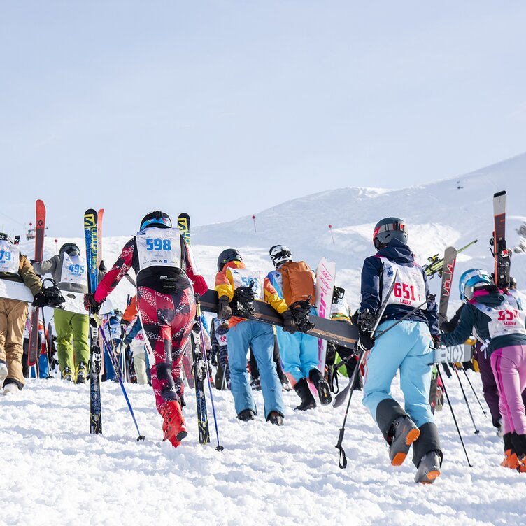 A group of skiers climbing a mountain in the St. Anton am Arlberg ski region, with bib numbers on their backs.