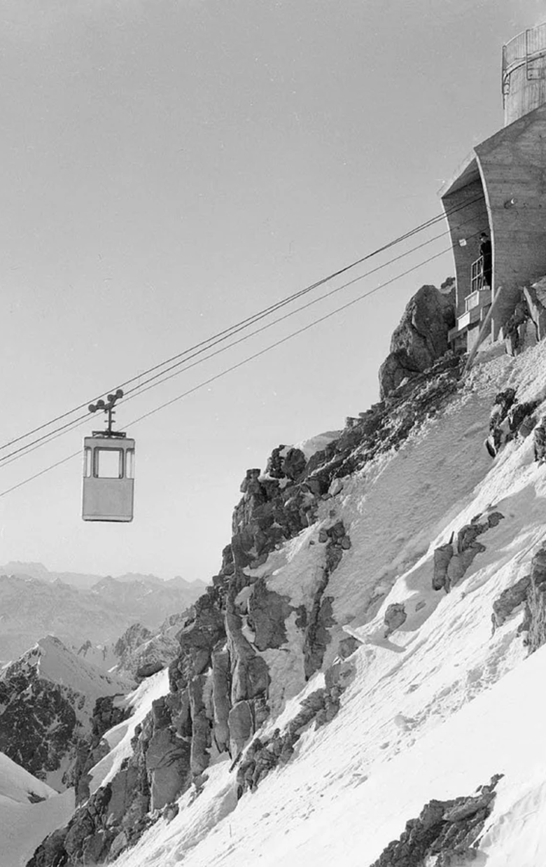 Cable car rides past steep snowy mountain slope.