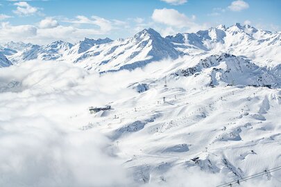 Skiregion St. Anton am Arlberg: verschneite Berge und Pisten unter einem klaren blauen Himmel, Wolken schwebend.
