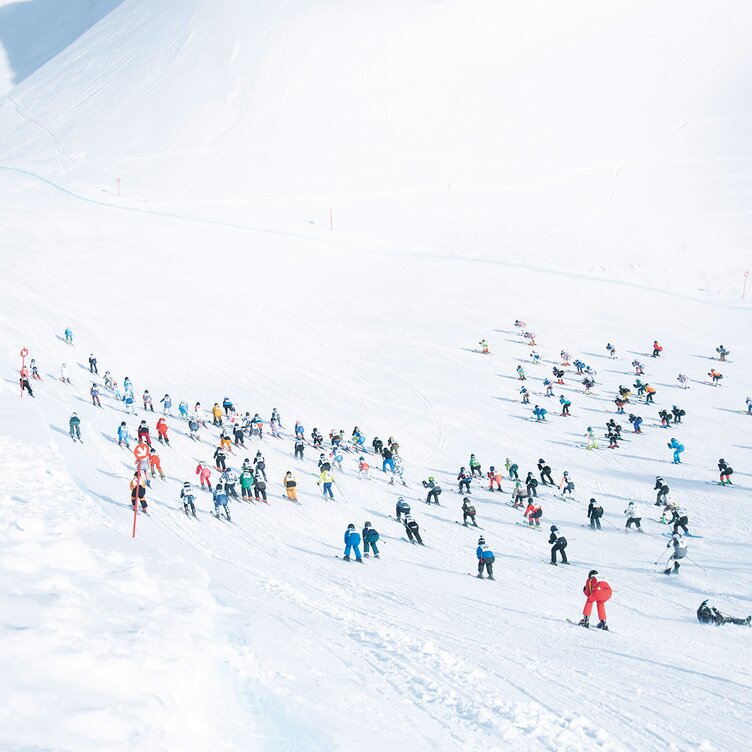 Many skiers simultaneously starting a descent on a snowy slope.