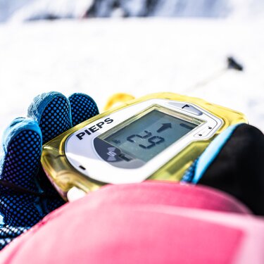 Hand hält ein Lawinenverschüttetensuchgerät im Schnee fest.
