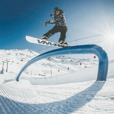 Snowboarder in Aktion auf einer blauen Rail im Stanton Park unter klarem Himmel.