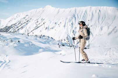 Skifahrer steht in schneebedeckter Landschaft mit Bergen im Hintergrund.