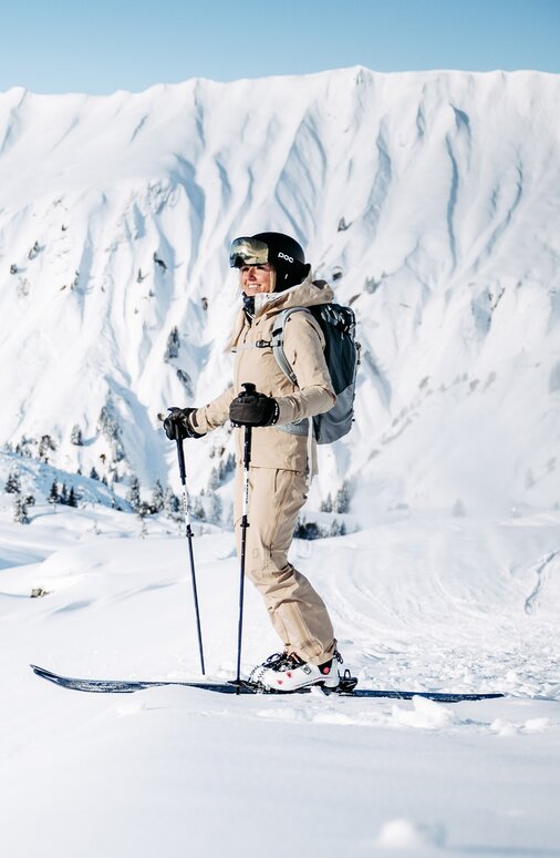Skifahrer steht in schneebedeckter Landschaft mit Bergen im Hintergrund.