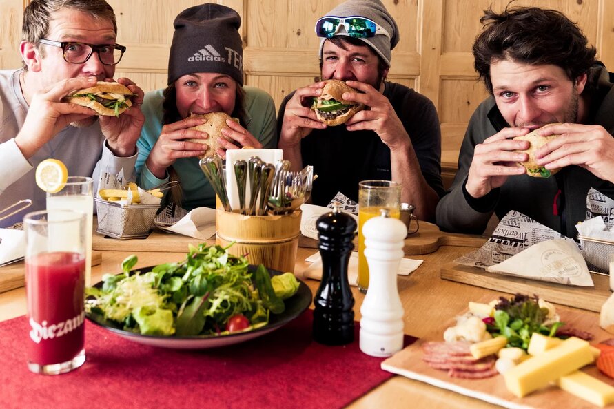 Vier Personen essen Burger an einem Tisch voller Speisen.