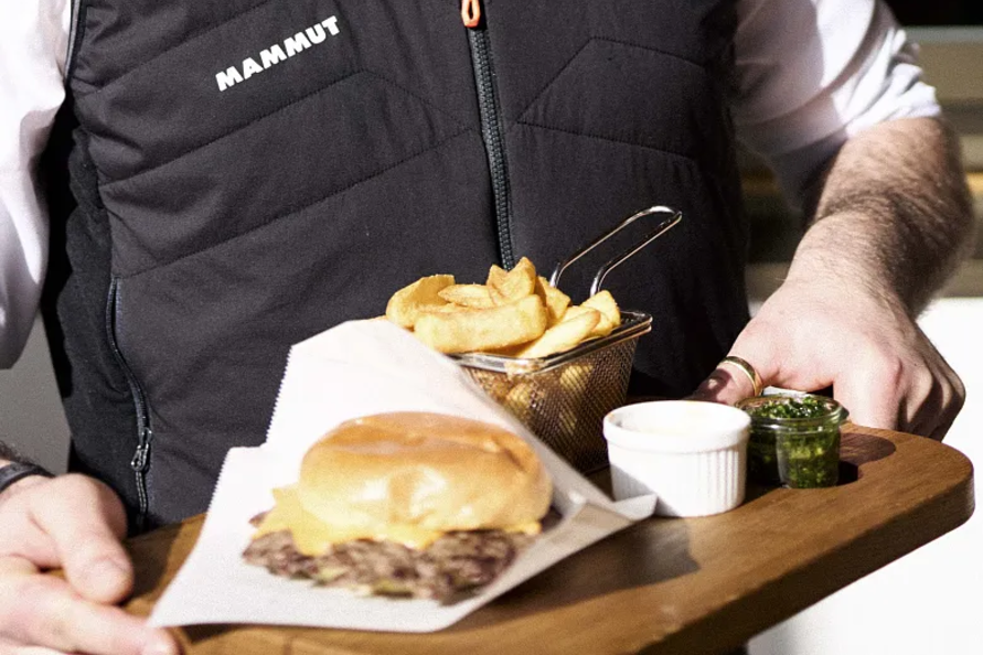 Person hält Tablett mit Burger, Pommes und zwei Dips.