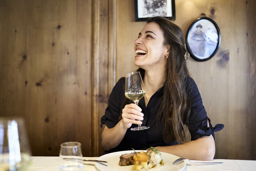 Eine Frau lacht herzlich mit einem Glas Weißwein in der Hand.