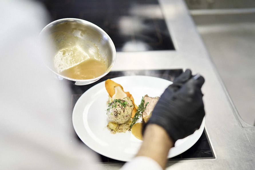 Koch richtet eine Speise in der Steffisalp Schirmbar mit Sauce aus einer Edelstahlkelle an.