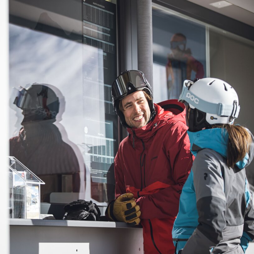 Two people in ski gear chatting at a snow counter.