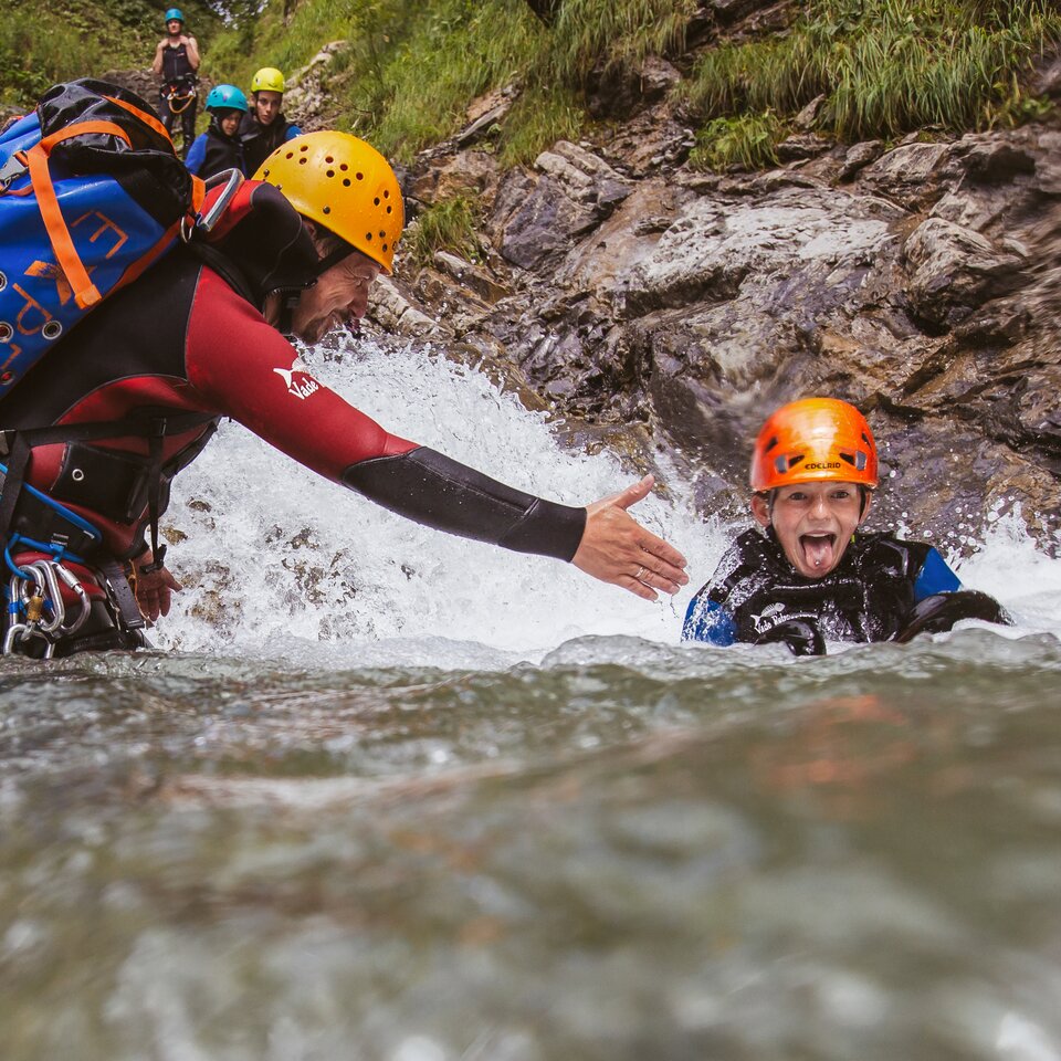 Erwachsener hilft einem Kind im Wildwasser beim Canyoning.