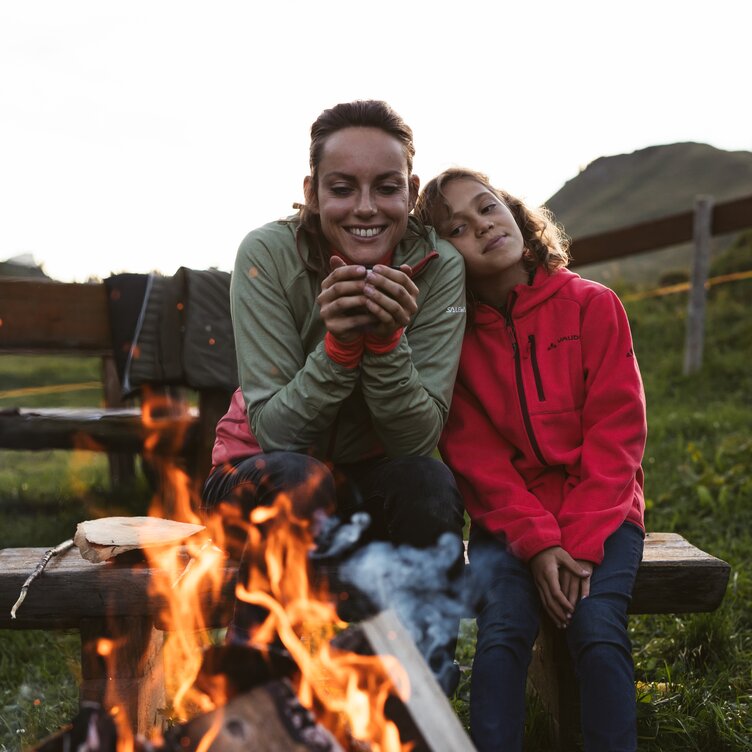 Two people enjoying a warm drink by an outdoor fire.
