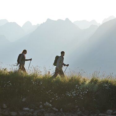 Two hikers with backpacks and poles on a mountain trail.