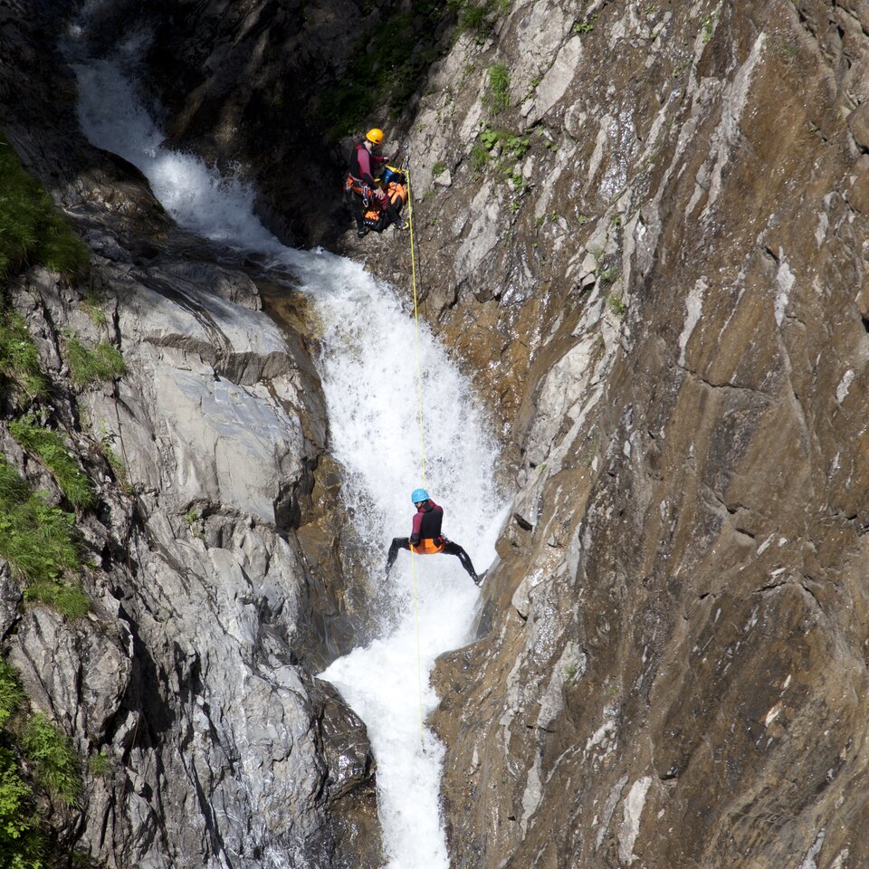 Two people rappelling down a rocky water gorge.