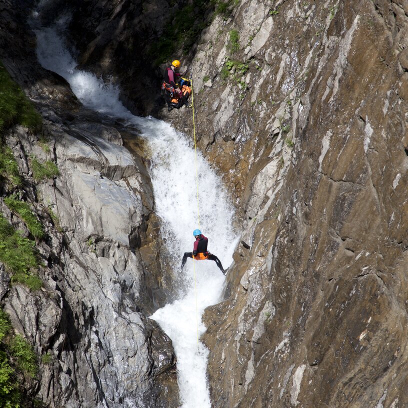 Zwei Personen seilen sich durch eine felsige Schlucht über dem Wasser ab.
