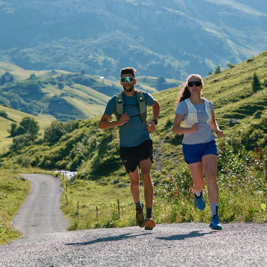 Zwei Personen laufen mit Rucksack auf einem Bergpfad Richtung Tal.