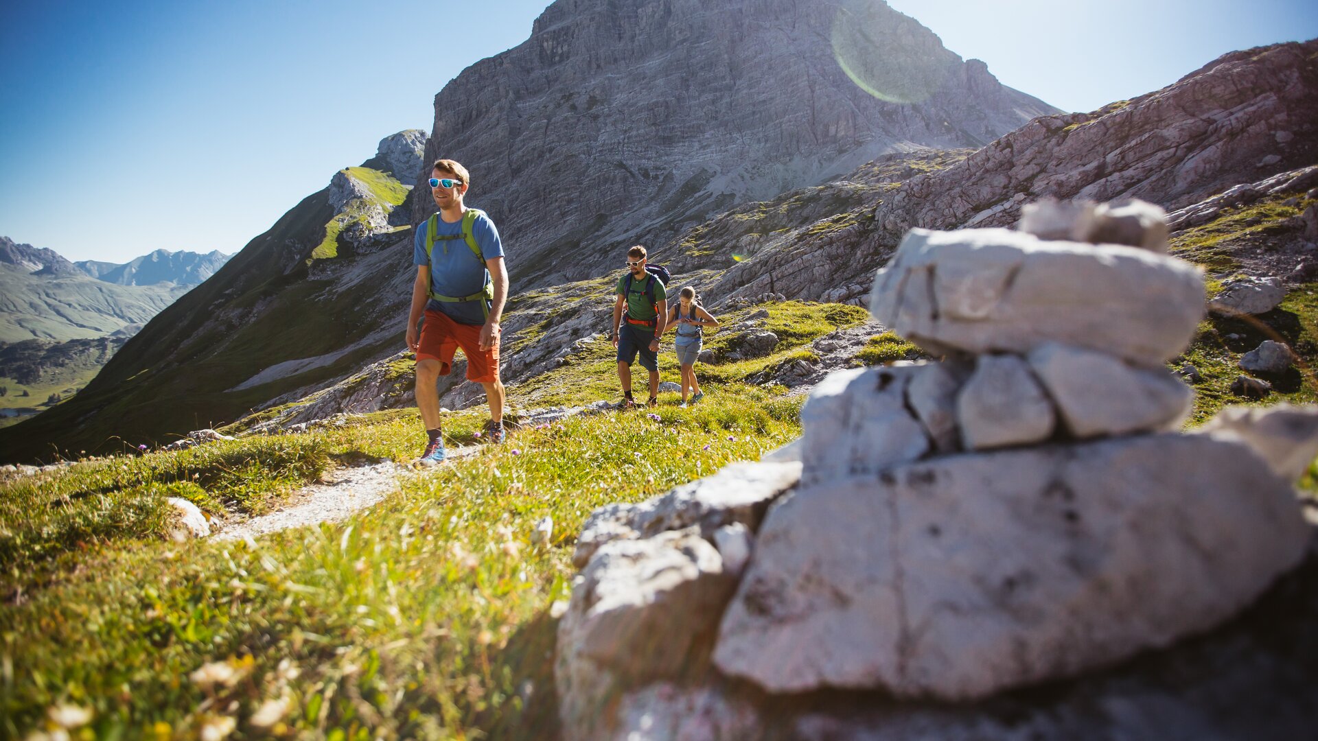 Group of people hiking on a mountain trail in sunlight.