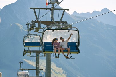 Ein Paar fährt in einem Sessellift mit Bergblick.