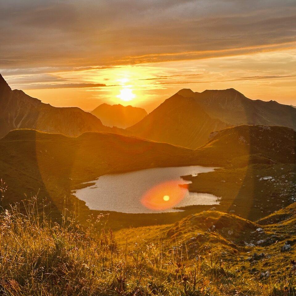 Ein atemberaubender Sonnenuntergang beleuchtet einen Bergsee und die umliegenden Gipfel mit goldenem Licht.