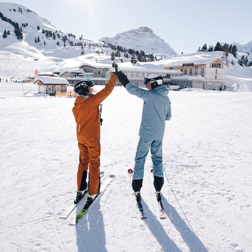 Zwei Skifahrer in farbiger Kleidung geben sich ein High-Five im Schnee.