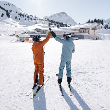 Zwei Skifahrer in farbiger Kleidung geben sich ein High-Five im Schnee.