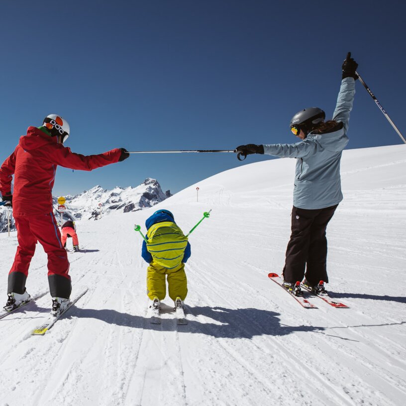 Eine Familie beim Skifahren in den Bergen unter blauem Himmel.