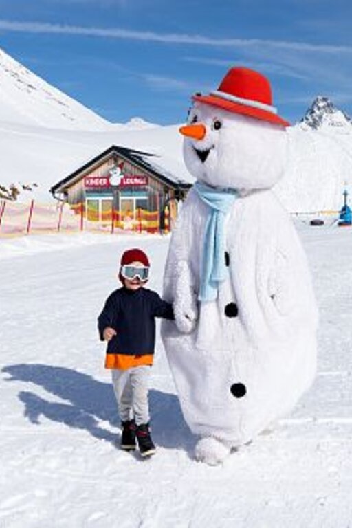Ein Kind und ein Schneemann-Maskottchen im Skiresort an einem sonnigen Wintertag.