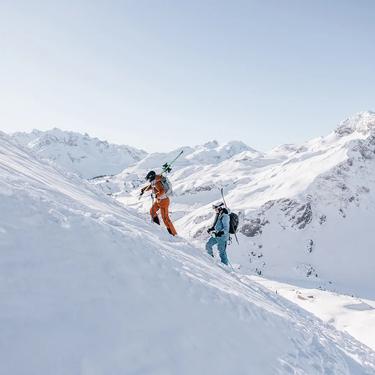 Zwei Skifreunde erklimmen eine verschneite Bergflanke.